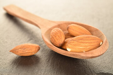 Several grains of peeled raw, organic almonds with a wooden spoon, close-up, on a slate board.