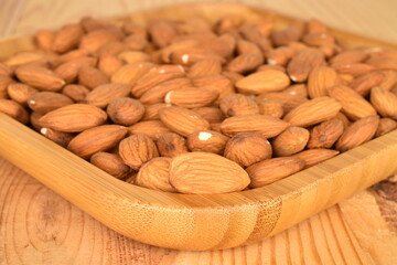Several grains of peeled raw, organic almonds in a bamboo plate, close-up, on a wooden table.
