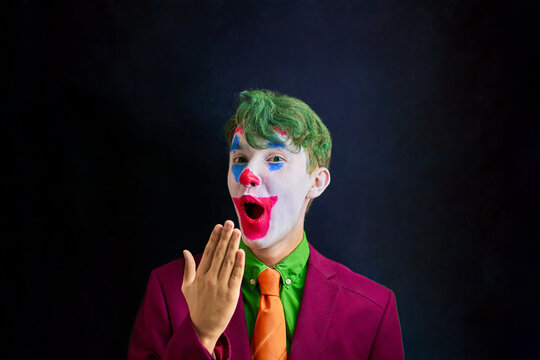 Man in mime makeup cosplay with green hair and a red suit an orange tie and a green shirt. Clown surprised or shocked