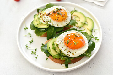 Fototapeta na wymiar Fried eggs, avocado and greens on toasted bread