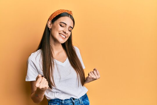 Beautiful brunette young woman wearing casual white t shirt very happy and excited doing winner gesture with arms raised, smiling and screaming for success. celebration concept.
