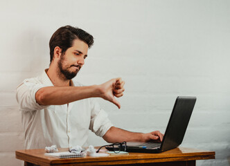 Young Caucasian male having a video call on a laptop and showing thumbs down disapproving gestures