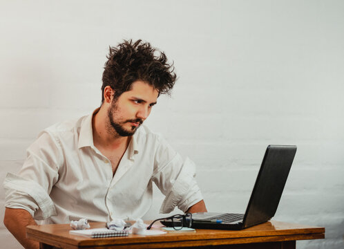 Young Caucasian male staring at the laptop, bored and disheveled during work