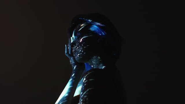Emotional crisis. Female loneliness. Night melancholy. Grief sorrow. Depressed sad woman crying in blue water rain drops on face skin from projector light isolated on black.