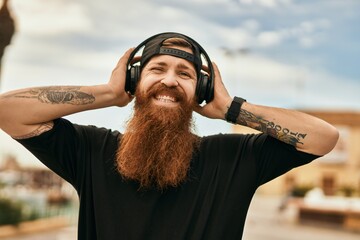 Young irish hipster man smiling happy listening to music using headphones at the city.