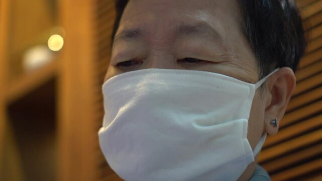 Asian senior lady wearing fabric mask looking tired