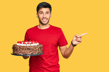 Young handsome man celebrating birthday with cake smiling happy pointing with hand and finger to...