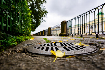 Rainy autumn day in the city, an alley in the park running along the embankment. Close up view of a hatch at the level of granite pavement