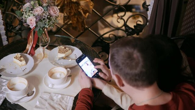 Couple in love sitting cafe table browsing mobile photo from romantic honeymoon. Newlyweds looking photo in smartphone from honeymoon trip in cafe