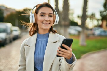 Young hispanic woman smiling happy using smartphone and headphones at the city.