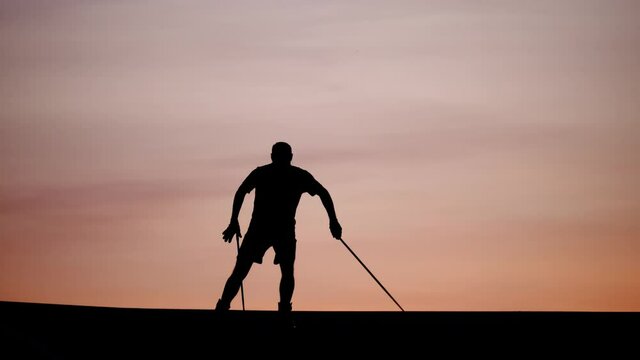 Man run on roller skis over hill top, training sportive skills or exercise at summer time. Silhouetted shot against cloudy evening sky, telephoto perspective