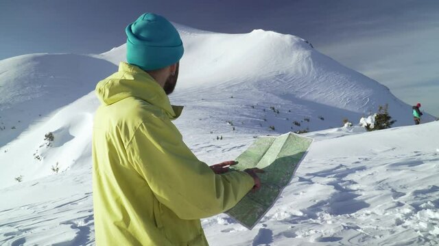 Bearded hiker finding way on paper map.  Panning shot of man overlooking mountain with glacier in winter. Concept of freedom and adventure
