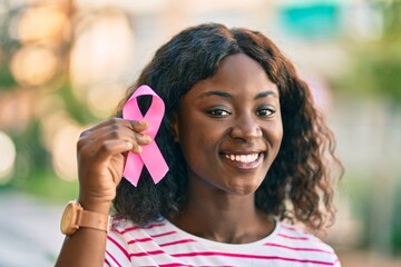 Young african american girl smiling happy holding pink breast cancer ribbon at the city. - Powered by Adobe