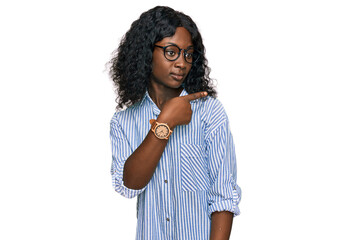 Fototapeta na wymiar Beautiful african young woman wearing casual clothes and glasses pointing with hand finger to the side showing advertisement, serious and calm face