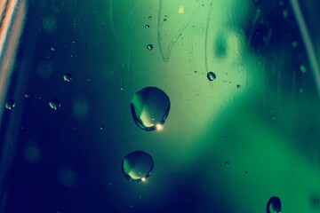 Macro photography of plastic bottle containing water, drops in the foreground, green color dominance.