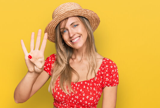 Beautiful caucasian woman wearing summer hat showing and pointing up with fingers number four while smiling confident and happy.