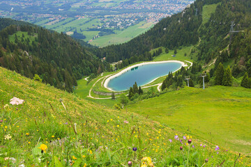 view from Brauneck mountain over flower meadow to artificial lake and Isar valley