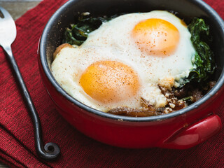 Baked eggs and spinach in a small baking dish on a red napkin.