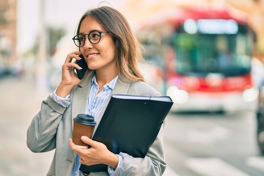 Young hispanic businesswoman talking on the smartphone and drinking take away coffee at the city.