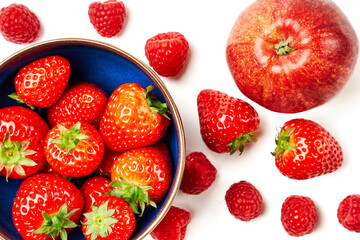 A blue bowl with strawberries and an apple, raspberries, strawberries on a white background.