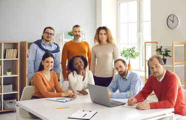 Corporate training. Confident and successful people group business team diverse community having meeting in office. Multiethnic smart casual coworkers standing or sitting at desk looking at camera.