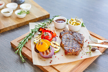 Grilled steak with baked vegetables on a wooden board on the table in the restaurant