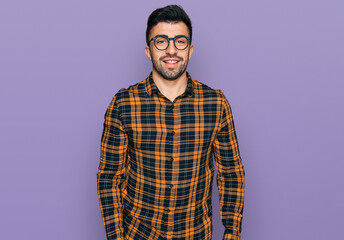 Hispanic man with beard wearing casual clothes and glasses looking positive and happy standing and smiling with a confident smile showing teeth
