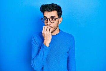 Young hispanic man wearing casual clothes and glasses looking stressed and nervous with hands on mouth biting nails. anxiety problem.