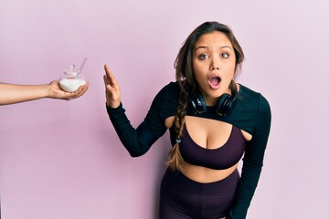 Young hispanic girl wearing sportswear rejecting bowl with sugar scared and amazed with open mouth...