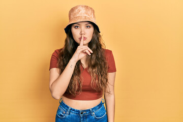 Young hispanic girl wearing casual clothes and hat asking to be quiet with finger on lips. silence...
