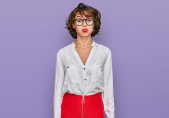 Young hispanic woman wearing business style and glasses puffing cheeks with funny face. mouth...