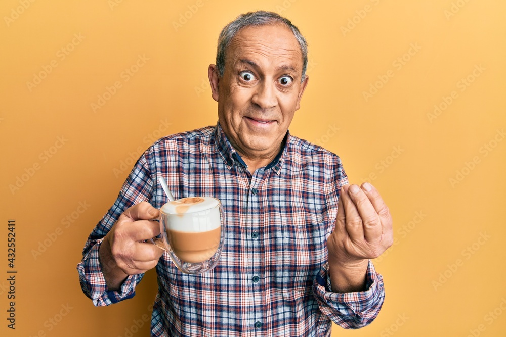 Sticker handsome senior man with grey hair drinking a cup coffee doing money gesture with hands, asking for 