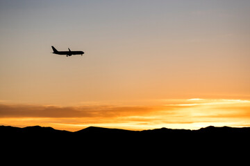 Naklejka na ściany i meble Silhouette of a jet plane over an orange sunrise over a mountain range