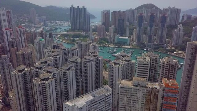 Aerial Shot Of Boats On Sea Amidst Buildings In City, Drone Ascending Forward Over Residential Structures On Sunny Day - Hong Kong, China