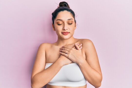 Beautiful middle eastern woman standing wearing a top showing skin smiling with hands on chest with closed eyes and grateful gesture on face. health concept.