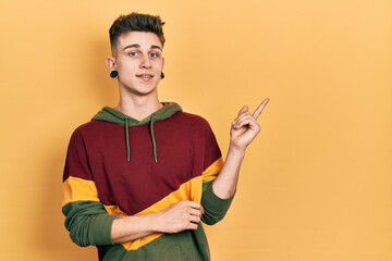 Young caucasian boy with ears dilation wearing casual sweatshirt with a big smile on face, pointing with hand and finger to the side looking at the camera.