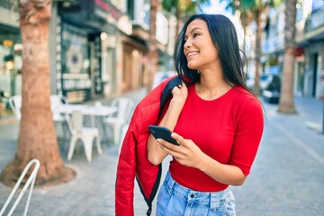 Young latin woman smiling happy using smartphone at the city.