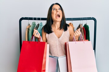 Middle age brunette personal shopper woman holding shopping bags angry and mad screaming frustrated...
