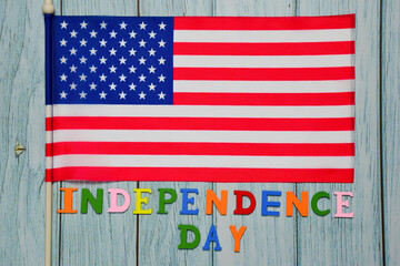 Under the US flag, the text INDEPENDENCE DAY is lined with multicolored letters on a wooden background.