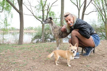 Young punk woman with her dogs in a park. Greyhound and chihuahua dogs.