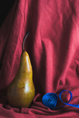A ripe pear on a red cloth background, next to a blue measuring tape. The concept of proper nutrition and a healthy lifestyle.