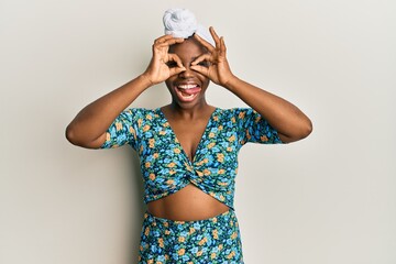 Young african woman wearing hair turban and african style doing ok gesture like binoculars sticking tongue out, eyes looking through fingers. crazy expression.