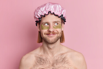 Skin care concept. Satisfied European man has mustache and bristle looks away stands topless indoor applies beauty patches under eyes refreshes face with vitamins isolated over pink background