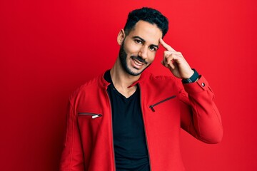 Young hispanic man wearing red leather jacket smiling pointing to head with one finger, great idea or thought, good memory