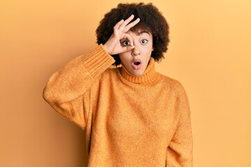 Fototapeta na wymiar Young hispanic girl wearing wool winter sweater doing ok gesture shocked with surprised face, eye looking through fingers. unbelieving expression.