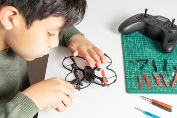Boy repairing the elices of his toy drone with a clamp in his hand and various tools and spare components on the table for his drone.
