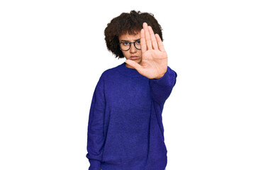 Young hispanic girl wearing casual winter sweater and glasses doing stop sing with palm of the hand. warning expression with negative and serious gesture on the face.