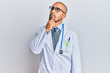 Hispanic adult man wearing doctor uniform and stethoscope with hand on chin thinking about question, pensive expression. smiling with thoughtful face. doubt concept.