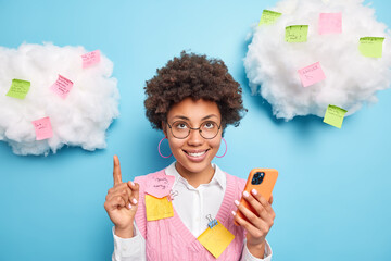 Smiling glad Afro American female office worker points upwards gives recommendations how to scheme...