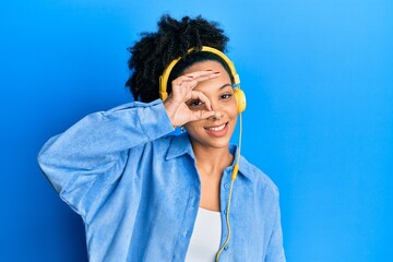 Fototapeta na wymiar Young african american girl listening to music using headphones smiling happy doing ok sign with hand on eye looking through fingers